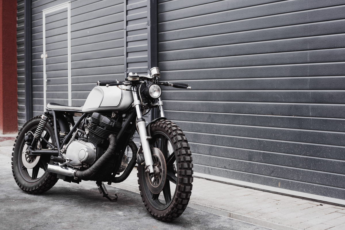 Grey rebuilt caferacer in front of rolled gates of garage. Wild lifestyle